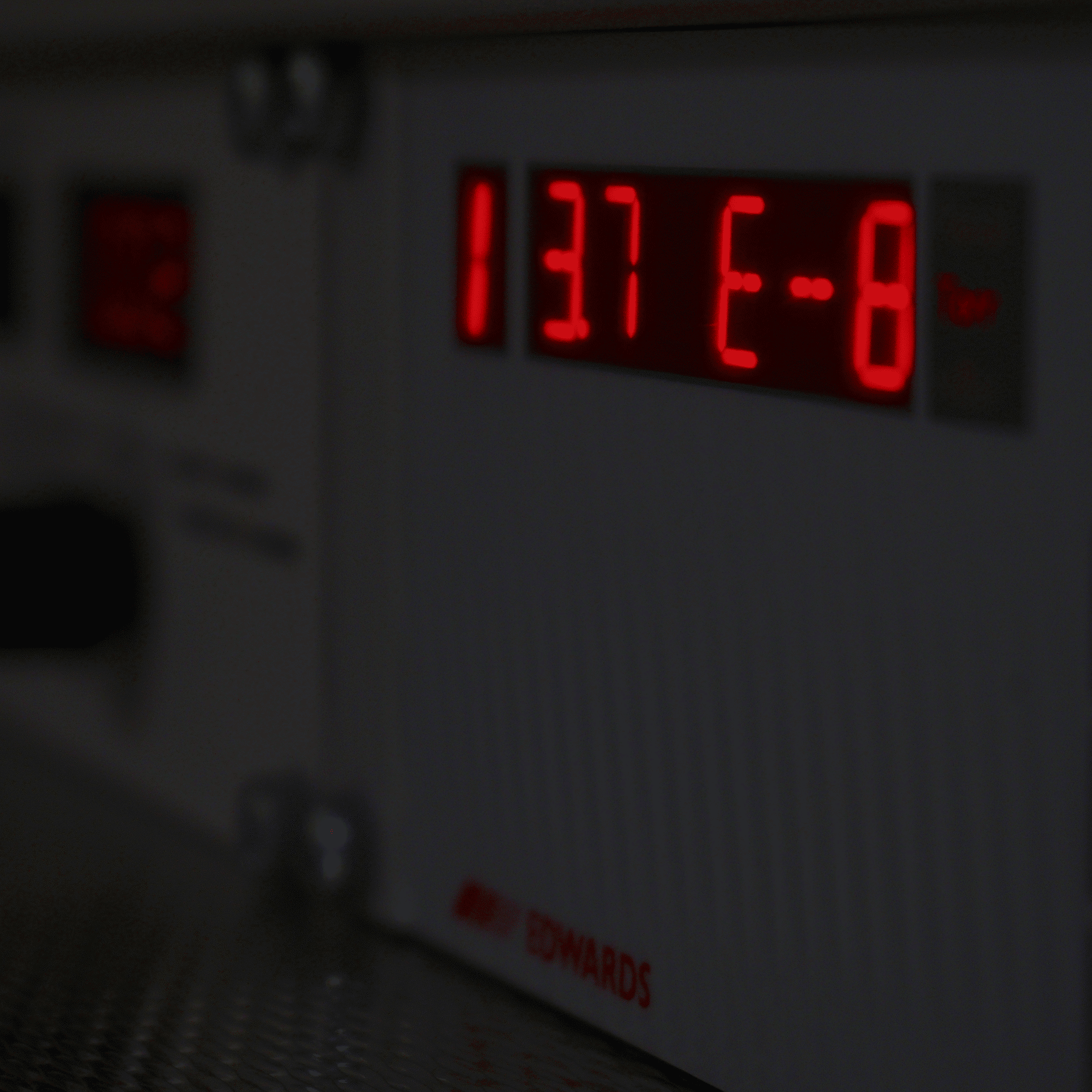 Close-up of a digital panel with red LED display showing "137 E-8". The panel is part of a scientific or industrial device, branded with "EDWARDS" in the lower part.
