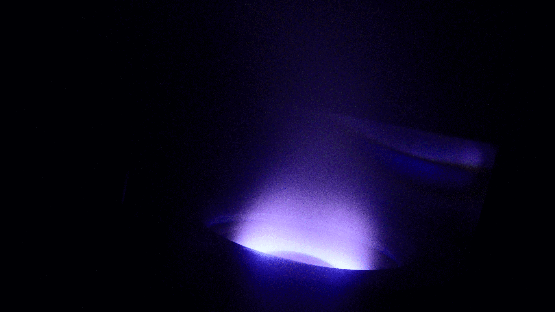 Blue and purple light glowing in a dark setting, emanating from an unidentified source at the bottom.